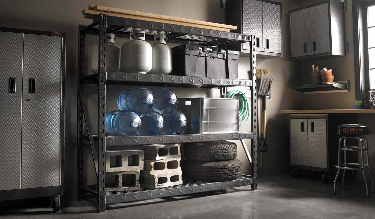 A Gladiator brand shelving unit stacked with concrete, water jugs, propane tanks and other heavy objects.